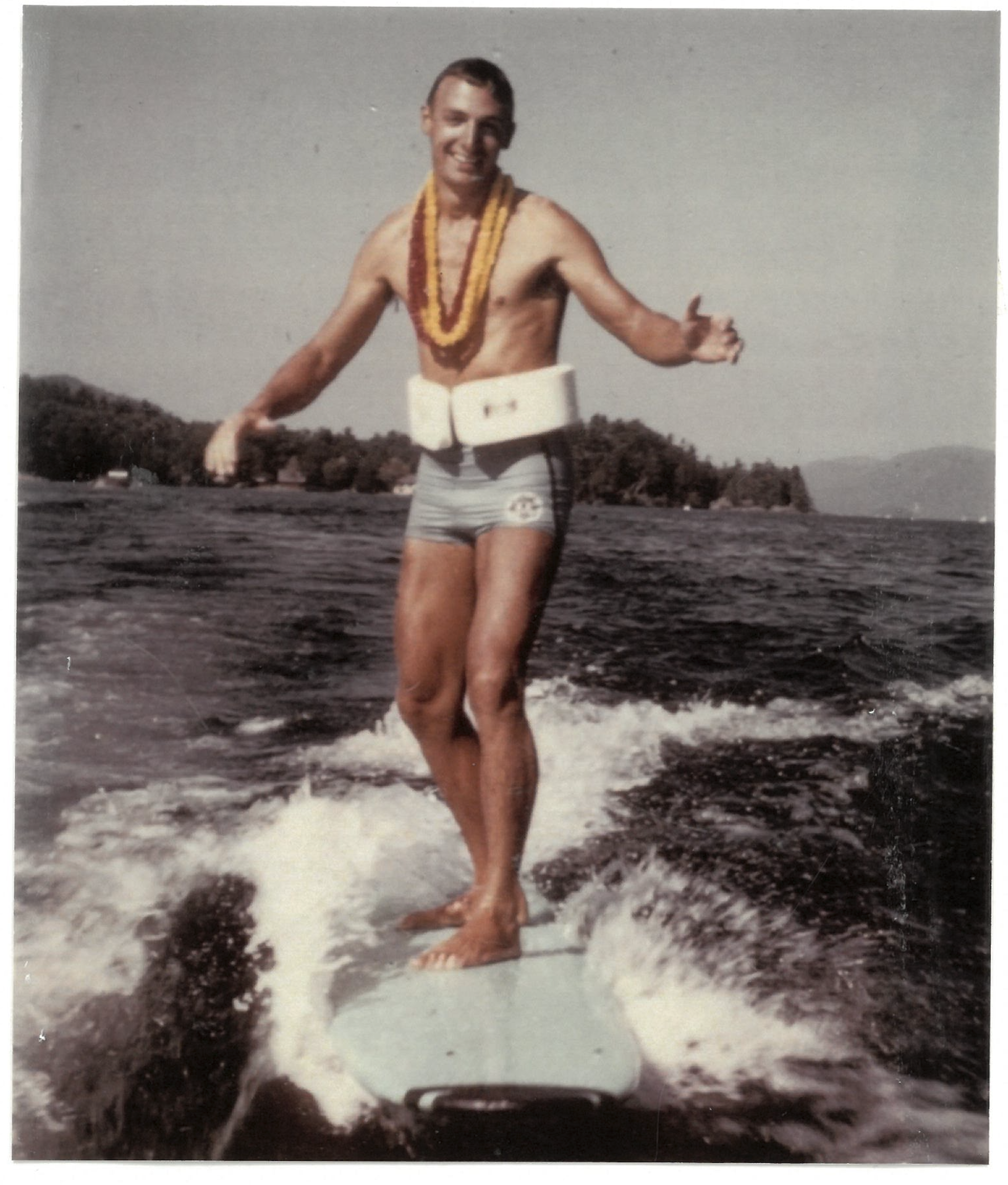 Photo of Tom Roach riding on a surf board behind a boat. 